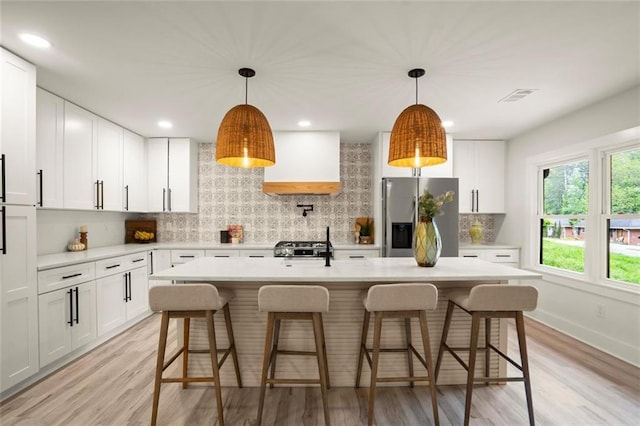 kitchen featuring stainless steel refrigerator with ice dispenser, light wood-type flooring, decorative backsplash, and light countertops