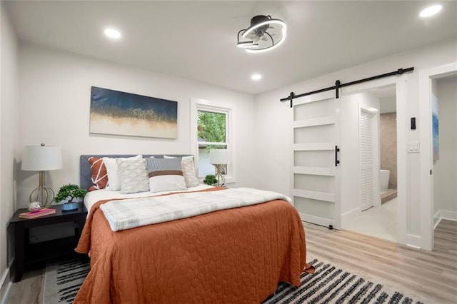 bedroom with light wood finished floors, recessed lighting, a barn door, and baseboards
