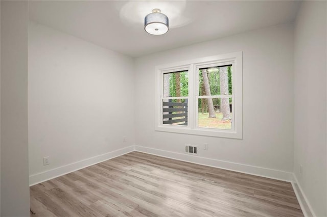 empty room with wood finished floors, visible vents, and baseboards