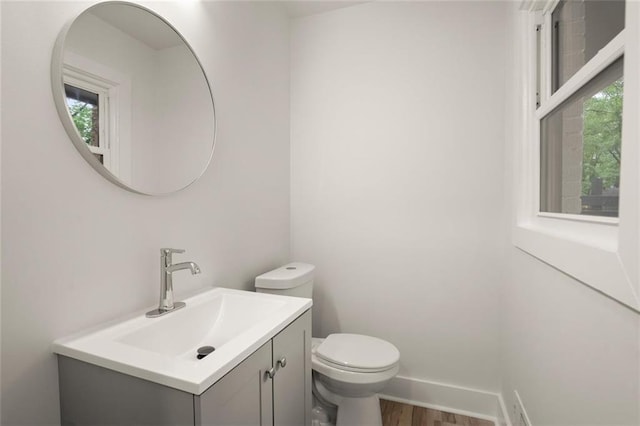 half bath featuring toilet, wood finished floors, vanity, and baseboards