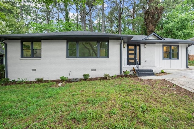 view of front facade featuring board and batten siding, a front yard, crawl space, and brick siding