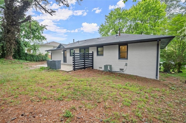 back of property with central AC, brick siding, and a yard