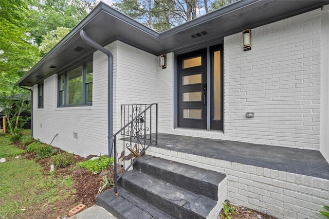 view of exterior entry featuring brick siding and crawl space