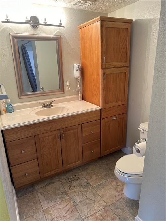 bathroom featuring toilet, a textured wall, a textured ceiling, and vanity