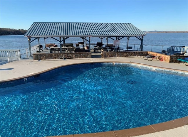 outdoor pool with a water view, a patio area, and fence