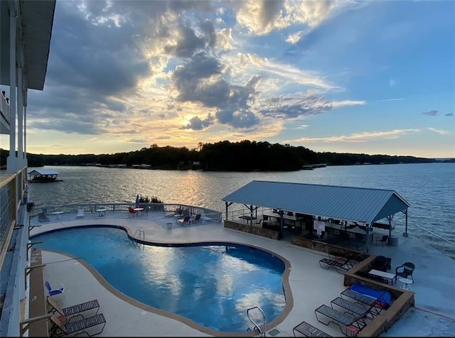 pool at dusk with a water view, a patio area, and a community pool