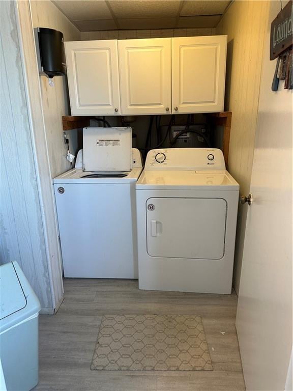 clothes washing area with washing machine and dryer, cabinet space, wood walls, and light wood finished floors