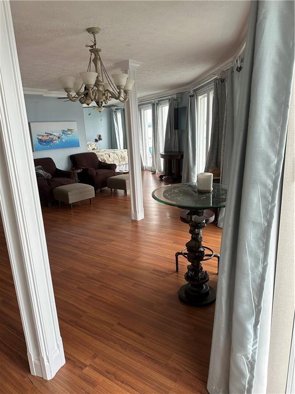 corridor with a textured ceiling, ornamental molding, a chandelier, and wood finished floors