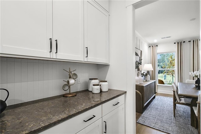 bar with white cabinetry, hardwood / wood-style floors, tasteful backsplash, and dark stone counters