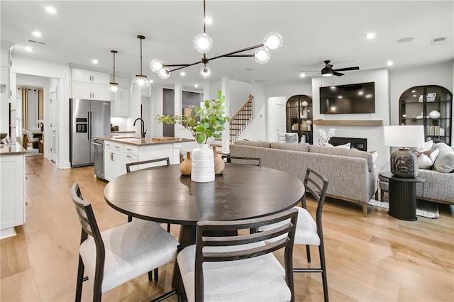 dining room with ceiling fan, light hardwood / wood-style flooring, sink, and a large fireplace