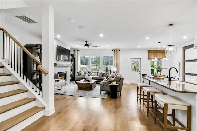 living room with ceiling fan with notable chandelier, a large fireplace, light hardwood / wood-style flooring, and sink