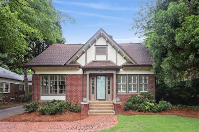 tudor house with brick siding, roof with shingles, stucco siding, and a front lawn