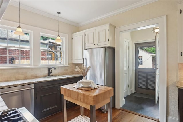 kitchen featuring a sink, stainless steel appliances, light stone countertops, plenty of natural light, and ornamental molding