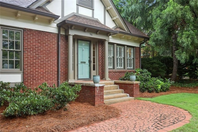 doorway to property featuring brick siding, stucco siding, and roof with shingles