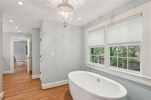 full bathroom featuring recessed lighting, baseboards, wood finished floors, a freestanding tub, and a chandelier
