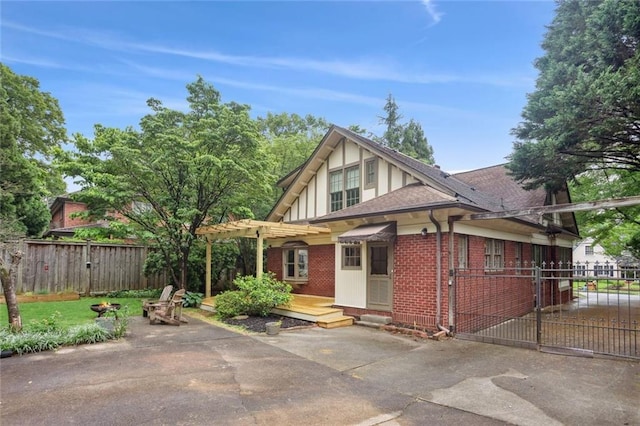 tudor-style house with a patio area, fence, brick siding, a pergola, and driveway