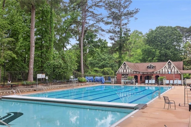 community pool featuring fence, view of scattered trees, and a patio area
