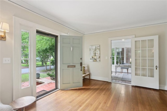 doorway to outside with hardwood / wood-style floors, plenty of natural light, baseboards, and crown molding
