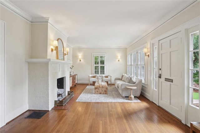 living area featuring hardwood / wood-style floors, ornamental molding, baseboards, and a brick fireplace