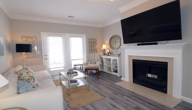 living area with visible vents, wood finished floors, a fireplace with raised hearth, and ornamental molding