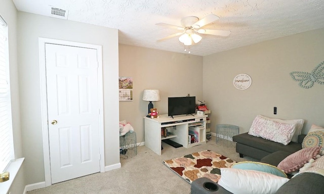 living area featuring light colored carpet, baseboards, visible vents, a ceiling fan, and a textured ceiling