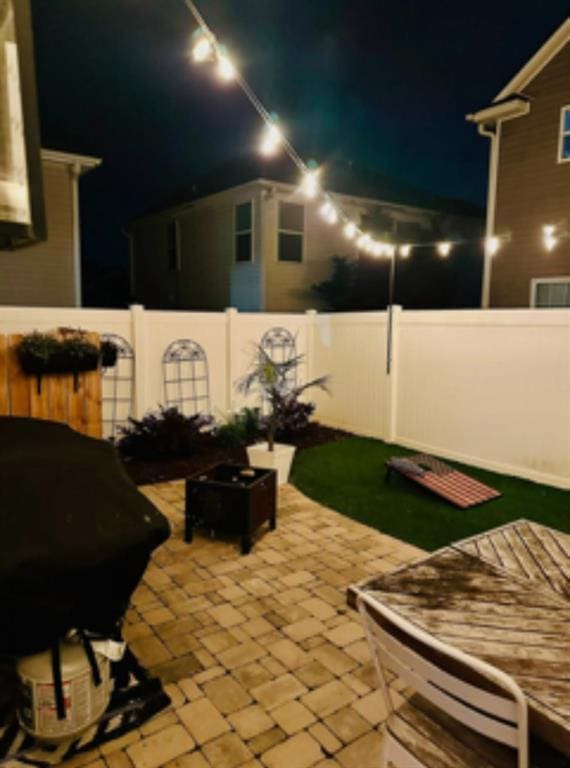 patio at night with a fire pit and a fenced backyard