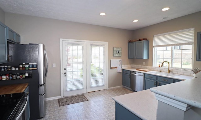 kitchen with stainless steel dishwasher, a sink, blue cabinets, and baseboards
