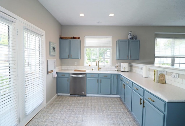 kitchen featuring stainless steel dishwasher, blue cabinetry, light countertops, and a sink