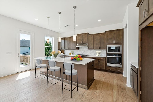 784 Keystone Dr, Woodstock, GA 30188 - kitchen with stainless steel appliances, under cabinet range hood, light wood-style flooring, backsplash, and light countertops