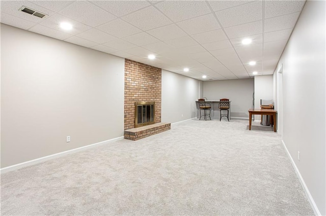 basement with carpet flooring, a paneled ceiling, bar area, and a fireplace