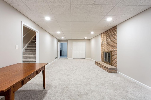 carpeted living room featuring a fireplace and a drop ceiling