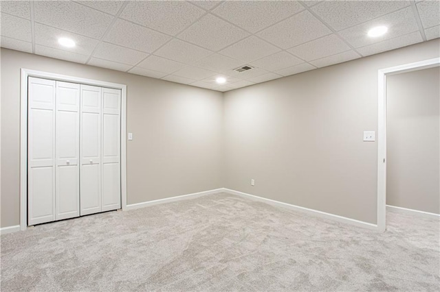 unfurnished bedroom featuring a drop ceiling, a closet, and carpet