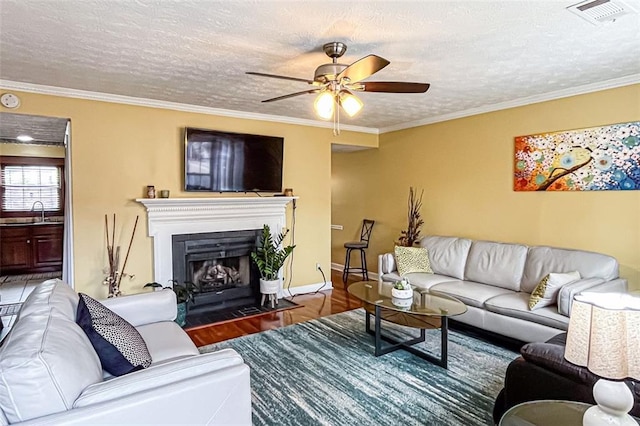 living room with sink, hardwood / wood-style flooring, ceiling fan, ornamental molding, and a textured ceiling