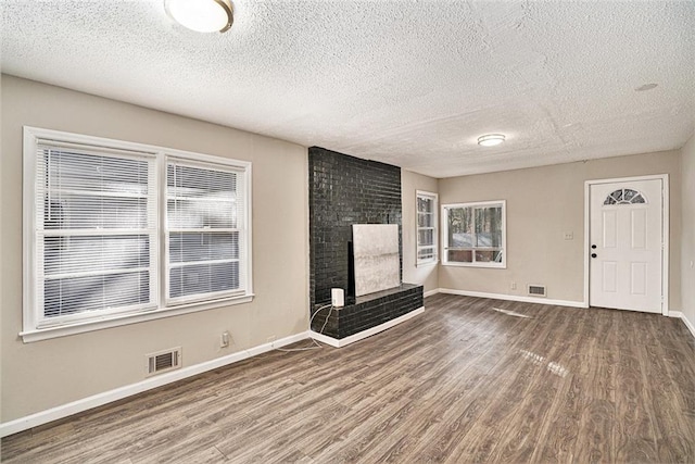 unfurnished living room featuring a brick fireplace, a textured ceiling, hardwood / wood-style floors, and a healthy amount of sunlight