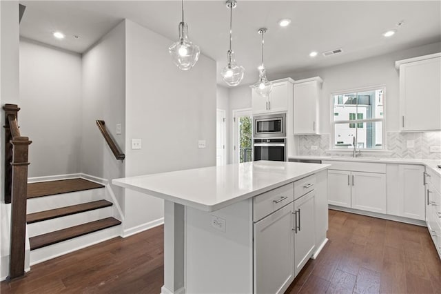 kitchen with appliances with stainless steel finishes, a kitchen island, white cabinetry, backsplash, and hanging light fixtures