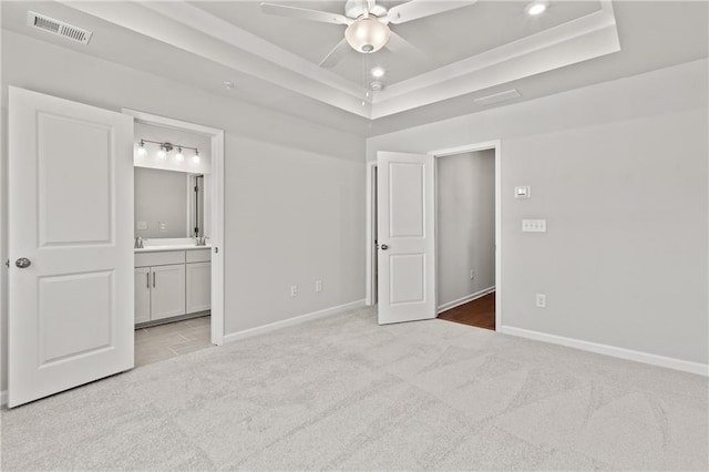 unfurnished bedroom with ceiling fan, connected bathroom, light colored carpet, and a raised ceiling