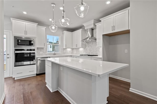 kitchen with pendant lighting, a center island, white cabinetry, wall chimney range hood, and stainless steel appliances