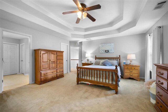 bedroom with ceiling fan, light carpet, and a tray ceiling