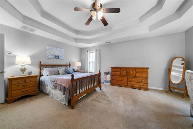 bedroom with light carpet, ceiling fan, and a raised ceiling