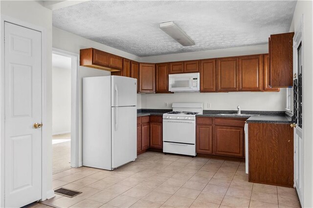 kitchen with a textured ceiling, sink, light tile patterned floors, and white appliances