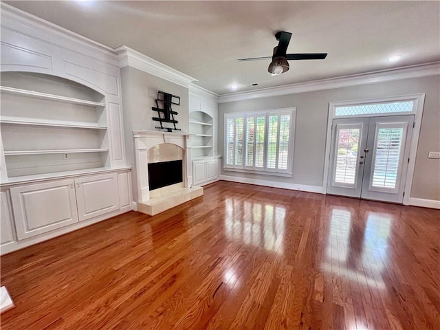 unfurnished living room with hardwood / wood-style flooring, ornamental molding, built in features, and french doors