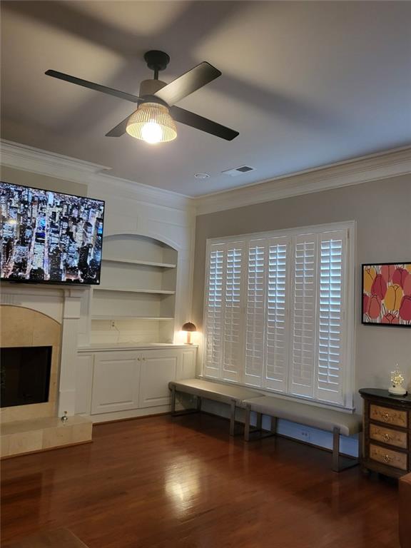 unfurnished living room featuring built in shelves, ornamental molding, dark hardwood / wood-style flooring, ceiling fan, and a high end fireplace