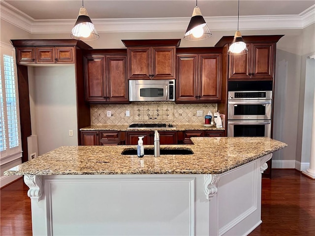 kitchen with stainless steel appliances, sink, hanging light fixtures, and a center island with sink