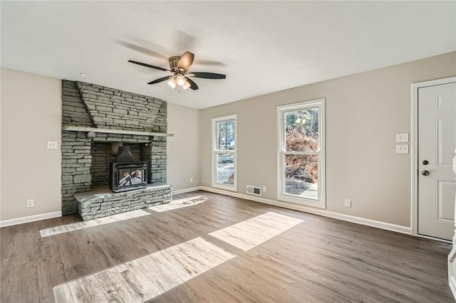 unfurnished living room with a wood stove, hardwood / wood-style floors, and ceiling fan