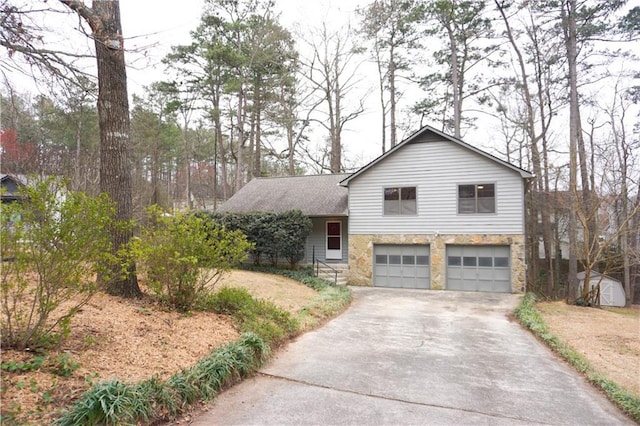 tri-level home with stone siding, an attached garage, and driveway