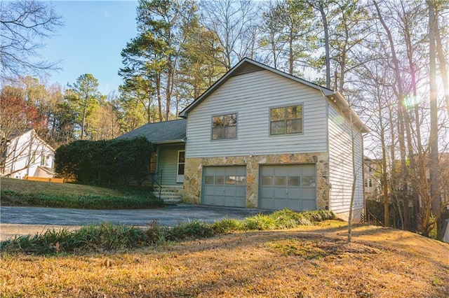 tri-level home with a garage, stone siding, and driveway