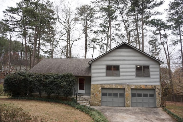 tri-level home featuring concrete driveway, an attached garage, stone siding, and a shingled roof