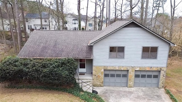 split level home featuring a garage, stone siding, driveway, and a shingled roof