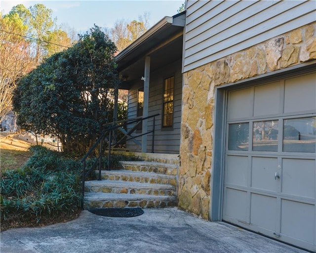 doorway to property with covered porch, stone siding, and a garage