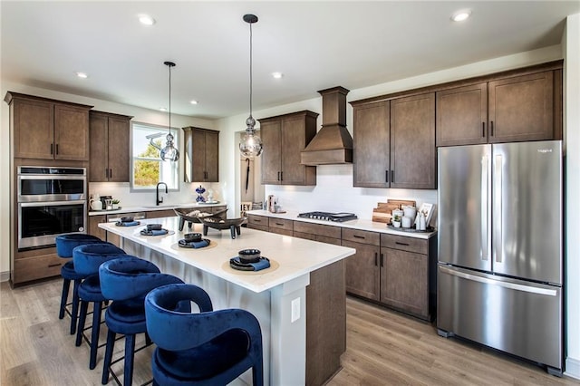 kitchen with a center island, custom exhaust hood, a breakfast bar, pendant lighting, and stainless steel appliances